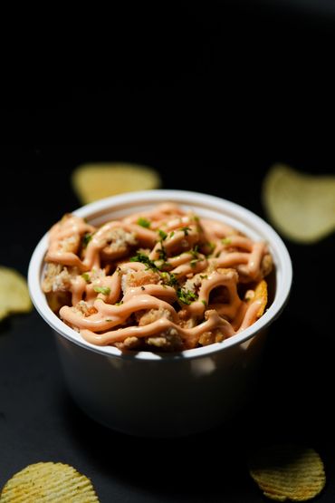 A bowl of crispy fried chicken topped with spicy mayo and herbs, surrounded by potato chips.