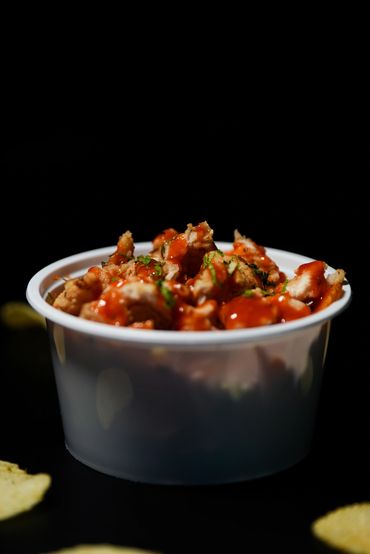 Cup of crispy chicken bites drizzled with spicy sauce.