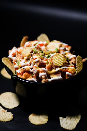 Loaded potato chips topped with sauces and herbs in a black bowl.