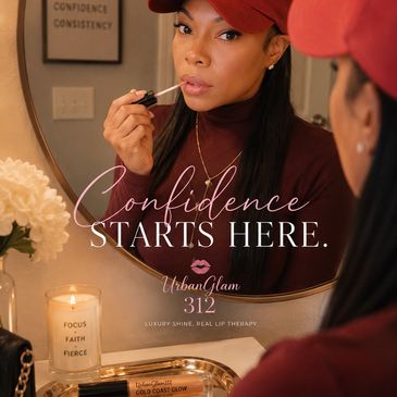 Woman applies lip gloss in mirror with confidence-themed decor.