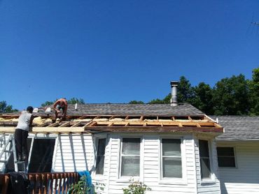 Two workers repairing the roof of a white house under a clear blue sky.