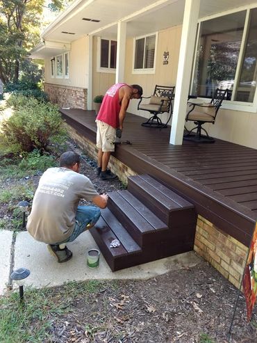 Two men painting and repairing a wooden porch and steps outside a house.