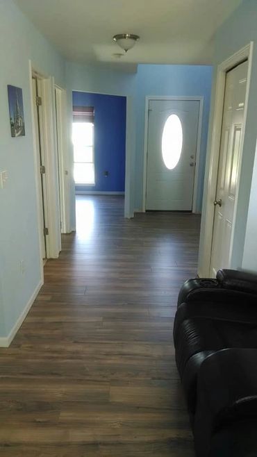 Bright hallway with wooden flooring and blue walls, featuring multiple doors and a black leather chair.