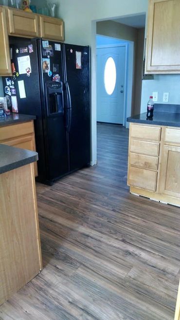 Modern kitchen with wooden cabinets, black refrigerator, and wood-look flooring.