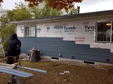 Worker installing blue siding on a house under construction.