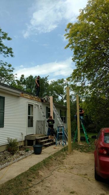 Three men working on house construction with ladders and wooden posts outside.