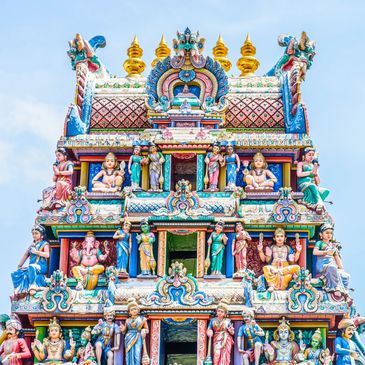 Colorful sculptures adorn a traditional Hindu temple tower against a clear sky.