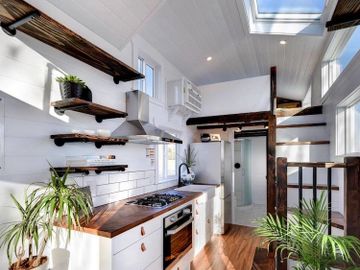 Tiny House with floating shelves, wood floors, a bedroom loft, full kitchen, and shiplap ceiling.