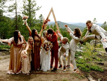 Joyful wedding party celebrates with laughter and playful poses in a scenic outdoor setting.