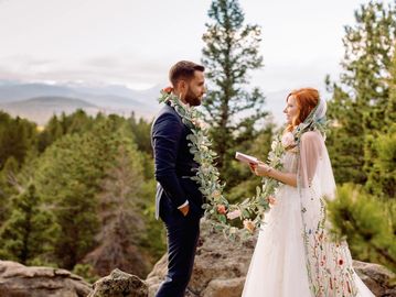 Couple exchanging vows outdoors with floral garlands in a serene forest setting.