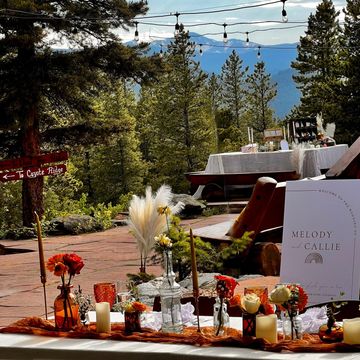 Outdoor wedding table decorated with flowers, candles, and pampas grass in a forest setting.