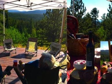 Two people enjoying drinks on a deck with forest and mountain views under a canopy.