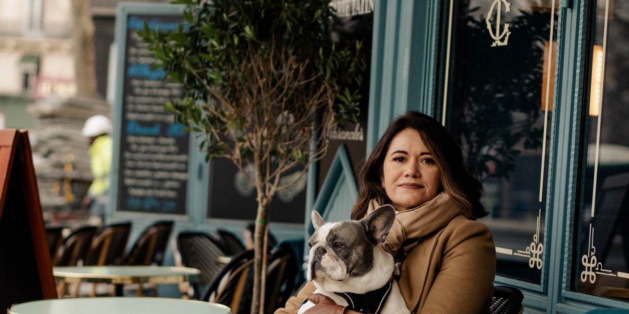 Woman holding a French Bulldog at an outdoor café in a cozy setting.