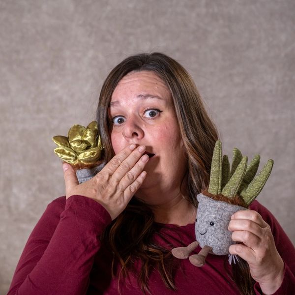 Woman with surprised expression holding two small handmade plant dolls. Headshot