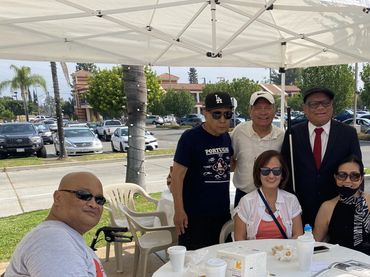 Group of six people sitting and standing around a covered table outdoors.
