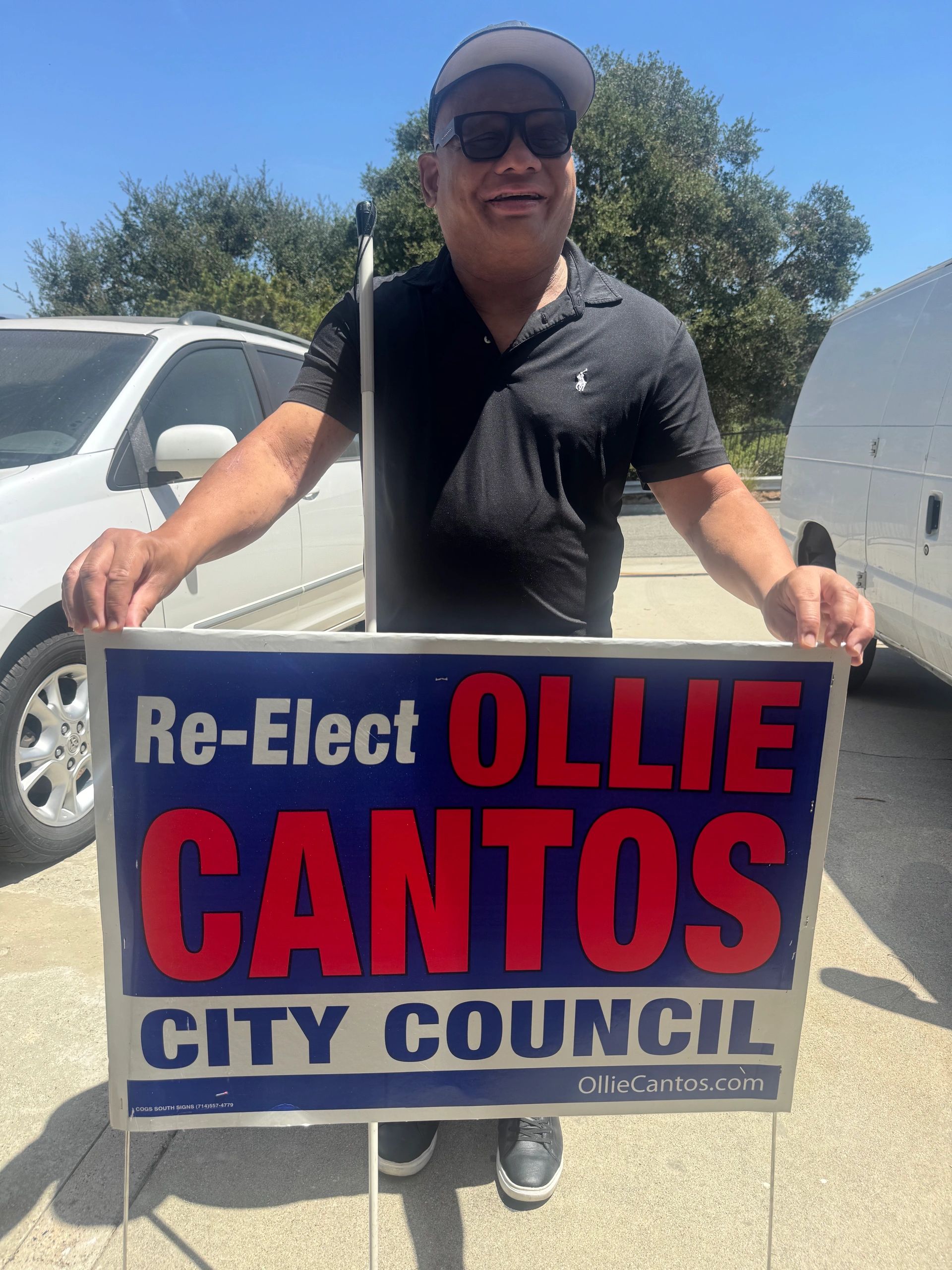 Ollie Cantos stands beyond his re-election campaign sign reading re-elect Ollie Cantos City Council.