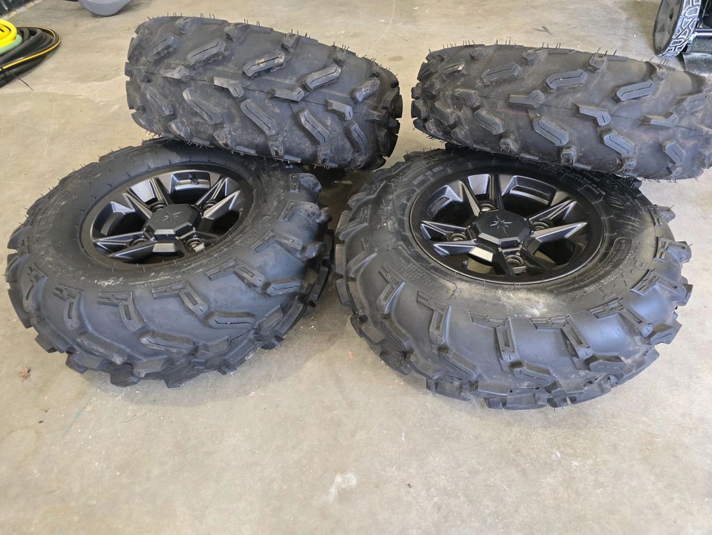 Four off-road tires with aggressive tread patterns and black rims on a concrete floor.