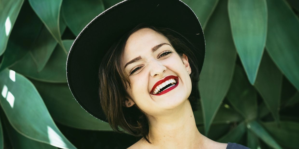 Laughing young woman in a black wide brim hat and dark red lipstick. FAQs are hilarious, apparently.