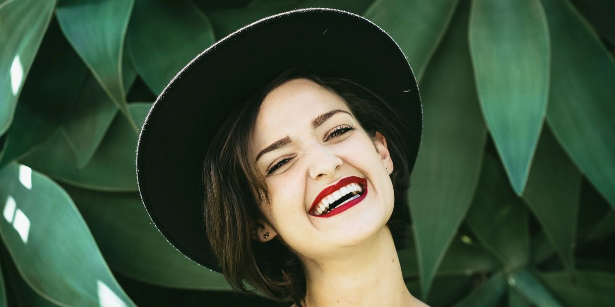 Laughing young woman in a black wide brim hat and dark red lipstick. FAQs are hilarious, apparently.