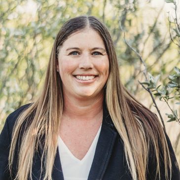 Smiling woman with long hair in a black blazer outdoors.