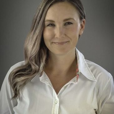 Smiling woman with long hair wearing a white shirt against a plain background.