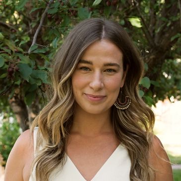 Smiling woman with wavy hair and boho earrings outdoors.