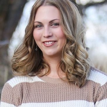 Smiling woman with curly hair wearing a striped sweater outdoors.