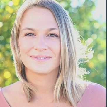 Portrait of a smiling woman with shoulder-length blonde hair outdoors in natural light.