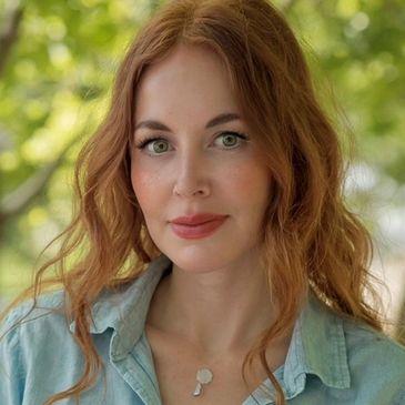 Portrait of a smiling woman with red hair and green eyes outdoors.