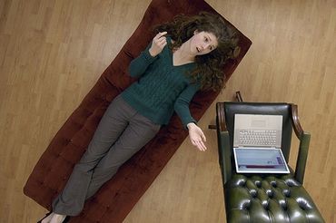 A woman lying on a chaise lounge talking, with a laptop on a nearby chair.