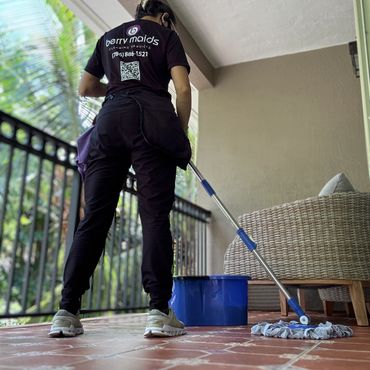 A cleaning service worker mops a tiled floor on a balcony.
