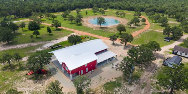 Aerial view of red barn and pond on green farmland.
