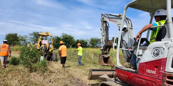 Construction workers operate heavy machinery in a field under a blue sky.