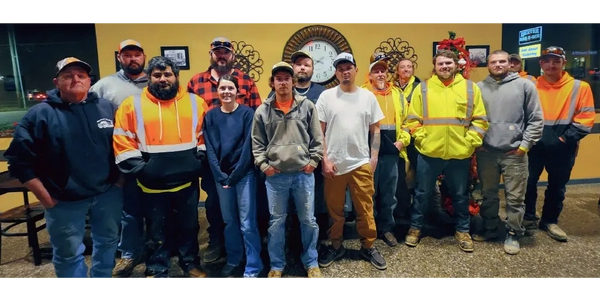 Group of workers posing indoors in front of a clock and holiday decoration.
