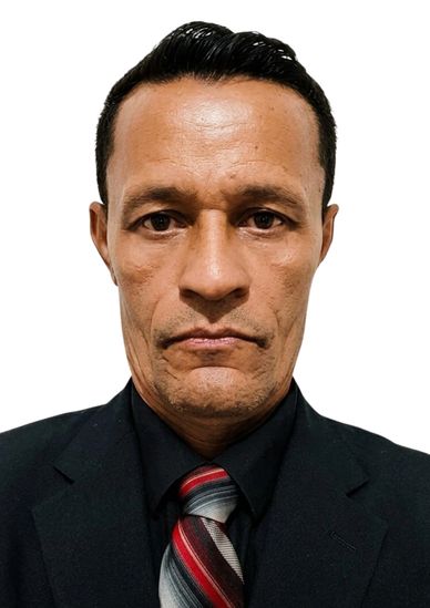 A serious man in a black suit with a striped tie, posing against a white background.