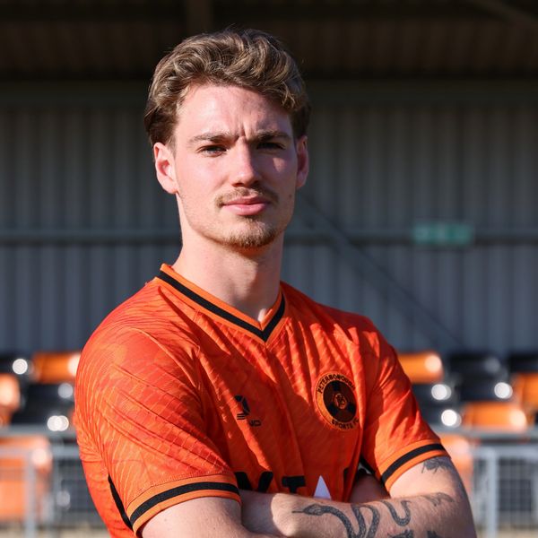 Young man in an orange sports jersey with arms crossed.