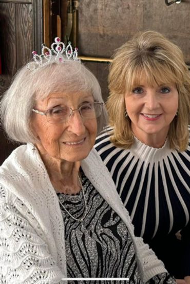 Two women smiling, one wearing a tiara and white shawl.