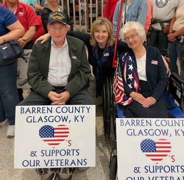 Two elderly veterans with a woman, holding signs supporting veterans in Barren County, KY.