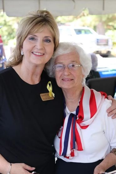 Two women smiling and embracing, one wearing a patriotic scarf.