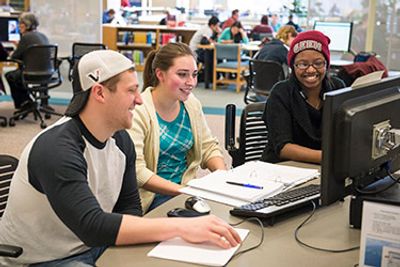 Three students collaborating around a computer in a library.