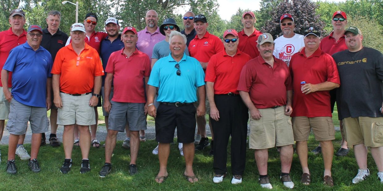 Group of men posing outdoors in casual attire, mostly wearing red shirts.