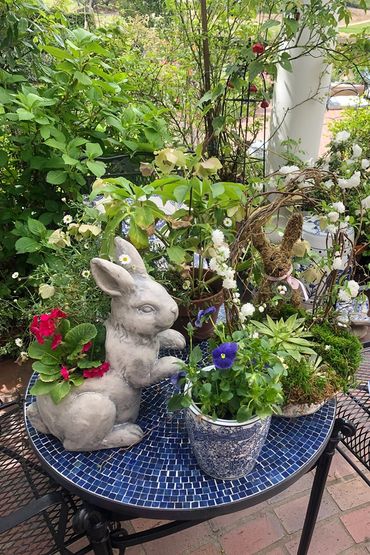 blue tile mosaic table with a ceramic rabbit and a selection of growing and flowering plants