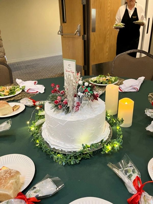 Centerpiece with lit up wreath around a white cake with holiday decorations on the top of the cake.