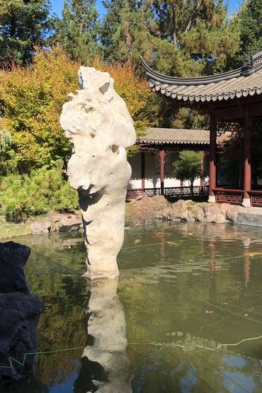 rock sculpture in a pond in front of a oriental pagoda