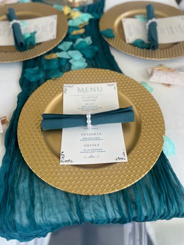 Elegant table setting with gold plates, teal napkins, and a detailed menu.