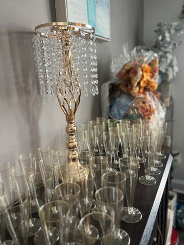 Elegant crystal chandelier and numerous empty champagne flutes on a dark wooden surface.