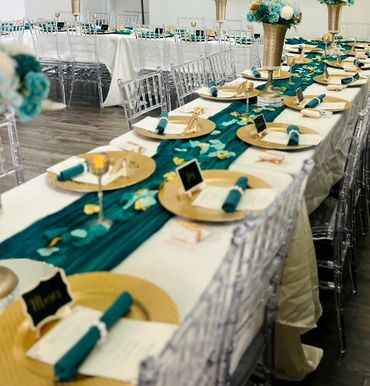 Elegant banquet table setup with teal and gold accents and clear chairs.