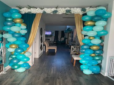 Colorful balloon arch with gold curtains decorating a hallway entrance.