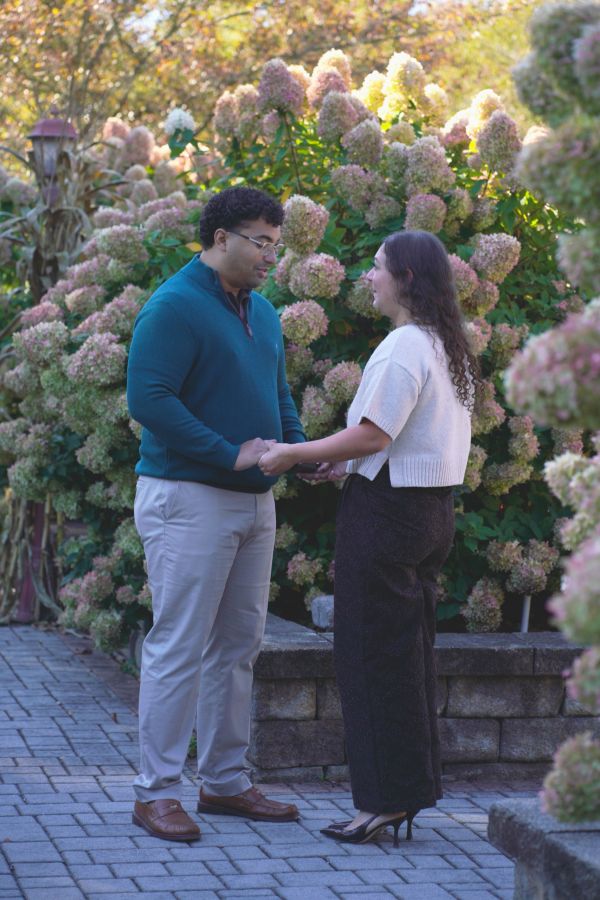 Couple holding hands outdoors near hydrangea bushes.