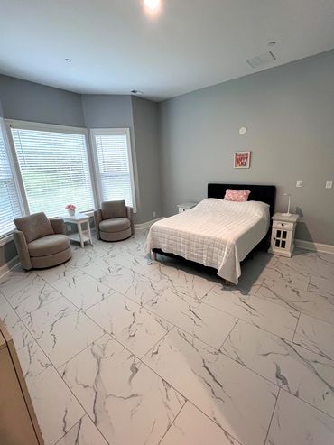 Minimalist bedroom with marble tile flooring, neutral tones, and cozy seating area by large windows.
